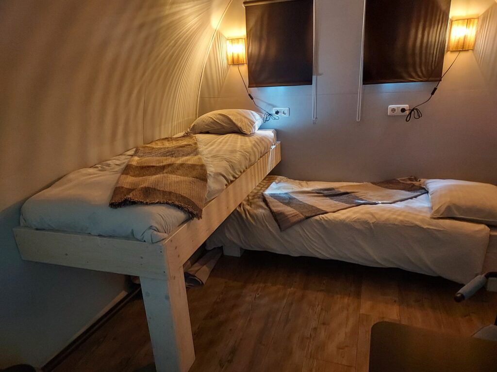 kampeerpod met twee éénpersoonsbedden, opgemaakt en bedlampjes aan