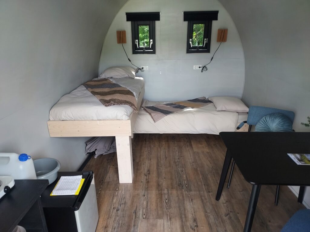 interieur in de kampeerpods. twee éénpersoons bedden, eethoek en kitchenette met campingkoelkast.